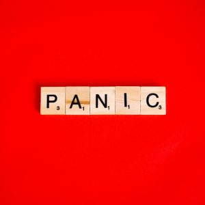 Scrabble tiles form the word 'panic' against a vibrant red backdrop, conveying urgency.